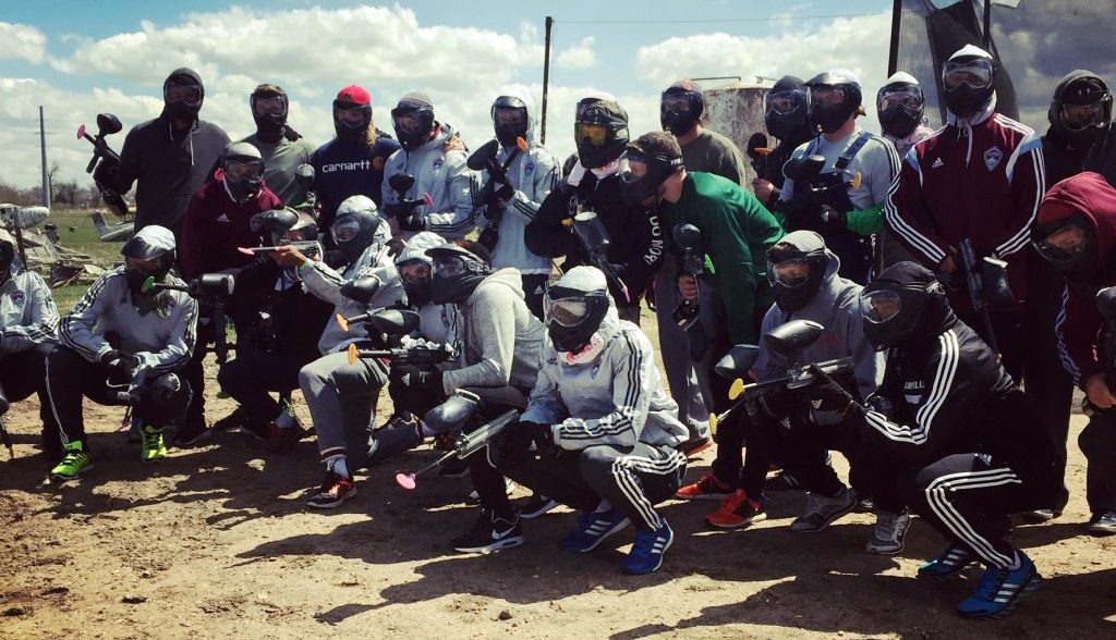 Large group of paintball players staged in rows standing and kneeling to pose for a picture at the outdoor paintball field.