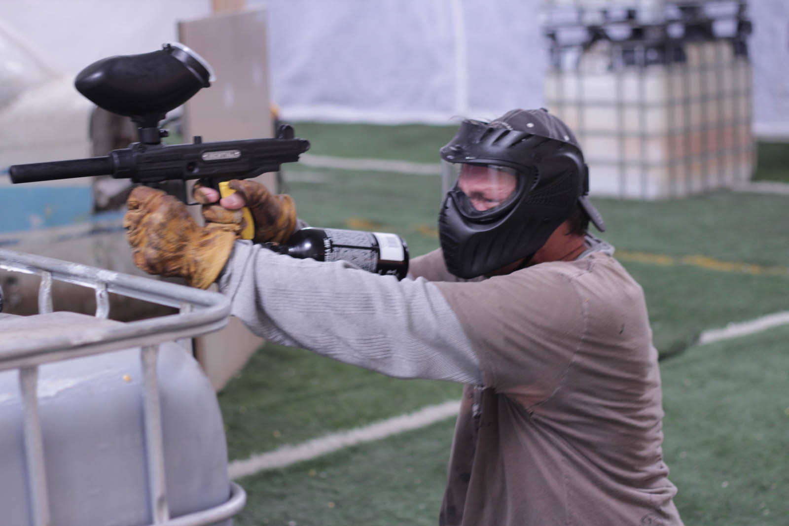 Paintball player behind a barrier in full gear propping his paintball gun up to shoot at the opponent in the indoor paintball field.